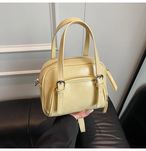 Dettaglio borsa in pelle lucida giallo chiaro con fibbie metalliche e cerniere lampo
