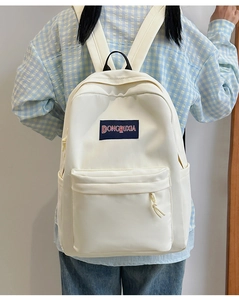 Detalle de mochila de lona crema con múltiples bolsillos y etiqueta de marca