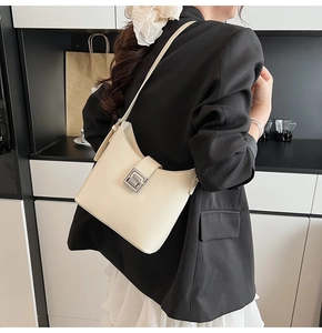 Close-up of minimalist beige shoulder bag with silver metal buckle on female model