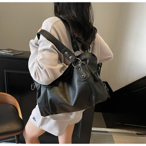 Detail of black pebbled leather tote bag with silver metal studs and wide shoulder strap