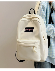 Detalle de mochila blanco roto con etiqueta tejida negra y bolsillo frontal con cremallera