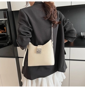 Modern cream patent leather shoulder bag with a silver buckle worn by a model in black blazer