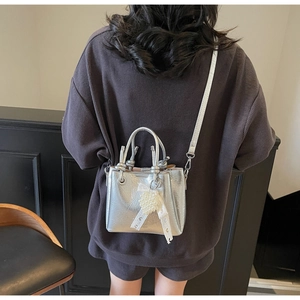 Detailed view of silver metallic bucket bag with pearl heart charm and lace ribbons