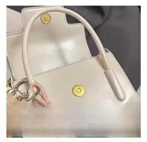 Detail of off-white leather handbag showing golden magnetic buckles and plush bear charm