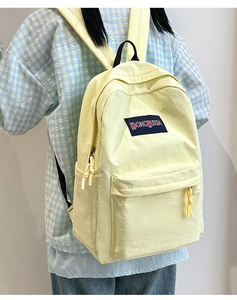 Detalle de mochila casual amarillo claro con bolsillo lateral y logo tejido frontal
