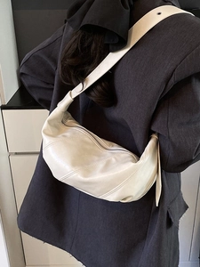 Cream-white crescent crossbody bag with diagonal stitching on a model in gray suit