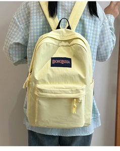 Vista detallada de la mochila amarilla ligera con bolsillo frontal y parche con logo azul