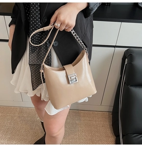 Detail of beige underarm bag with silver chain and metal buckle shown on a model