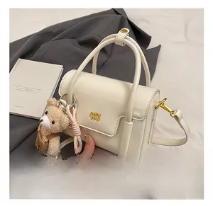 Detailed view of cream PU leather handbag with gold logo and plush bear charm