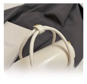 Detailed close-up of cream leather mini handbag with gold metal logo and round dual handles