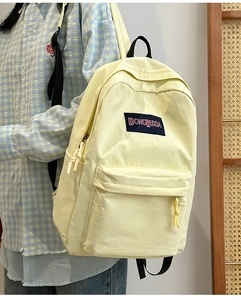 Detalle de mochila amarillo claro con bolsillo frontal con cremallera y logo textil