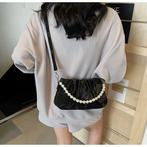 Detail view of black pleated cloud bag featuring large pearl chain and adjustable strap