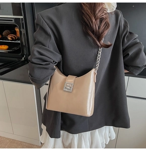 Detail of cream patent leather underarm bag with silver chain strap and metallic buckle