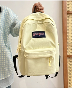 Detalle de la mochila de nailon amarillo claro con bolsillo frontal y parche con logo