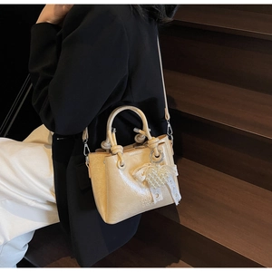 Detail of cream pleated shoulder bag featuring a pearl heart pendant and silver hardware