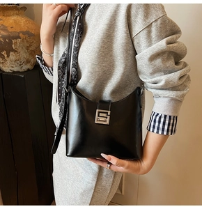 Detail of black leather shoulder bag featuring a silver square buckle and printed silk scarf