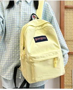 Detalle de mochila de nailon amarillo con correas laterales y parche de logo DONGRUXIA