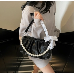 Close-up of black pleated cloud bag featuring pearl chain and white lace bow detail