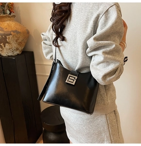 Detail of a minimalist black polished leather shoulder bag with a square metal buckle