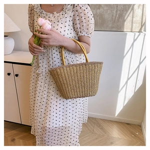 Detail of yellow woven straw tote bag held by model wearing a floral dress