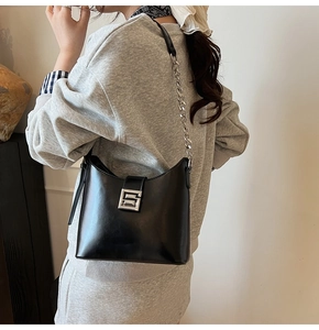 Detail of black glossy leather bag with silver buckle and metallic chain strap