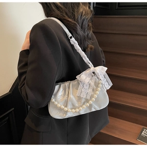 Detail of silver pleated cloud bag with pearl strap and lace bow on a black blazer