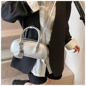 Détail du sac à main argenté métallisé avec breloque cœur porté par un mannequin