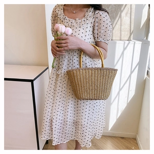 Close-up of a hand-woven straw tote bag held with fresh pink tulips in a natural setting