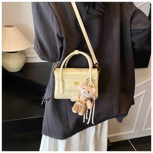 Detail of beige patent leather handbag with gold logo and cute teddy bear charm