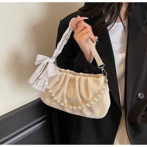 Close-up of pleated cream shoulder bag with pearl chain strap and lace bow detail