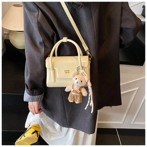 Detail view of cream square handbag with gold logo and plush bear charm on a model