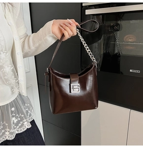 Detail of dark brown glossy patent leather saddle bag with silver chain and metal buckle