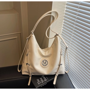 Détail d'un grand sac hobo beige avec logo M en métal posé sur un banc en cuir noir