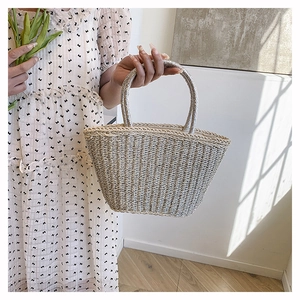 Detail of woven straw tote bag featuring circular top handles and shimmering texture