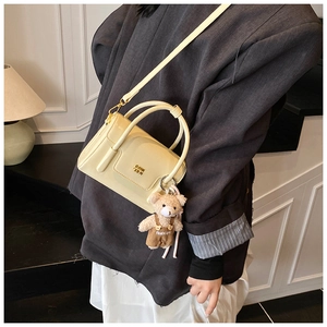 Detail of cream crossbody bag with golden CDIN logo and a cute teddy bear charm