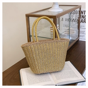 Close-up of woven straw tote bag with circular gold metal handles on a wooden table