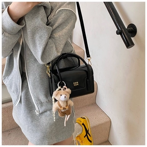Detail of black patent leather crossbody bag with gold logo and cute bear plush charm