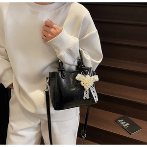 Detail of black patent leather bucket bag with white lace bow and pearl accents