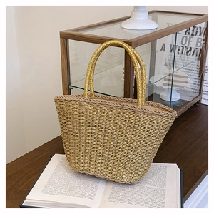 Vue détaillée d'un sac cabas en paille tressée dorée pour les vacances sur un livre