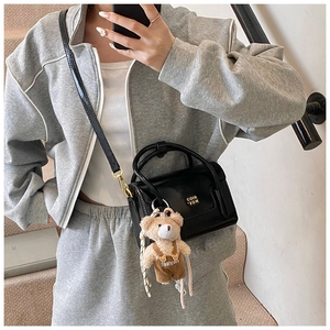 Detail of black glossy leather square bag with a cute khaki teddy bear plush pendant