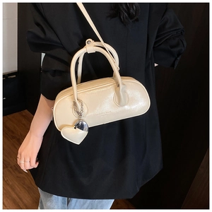 Détail d'un sac bowling en cuir crème avec pendentif cœur porté sur une tenue noire