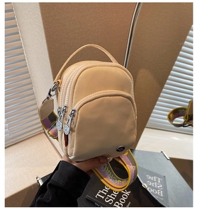 Détail du sac bandoulière en nylon beige avec trois zips et une sangle tissée colorée
