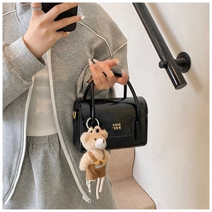 Detail einer schwarzen glänzenden Mini-Tasche mit süßem Teddy-Anhänger und Gold-Logo