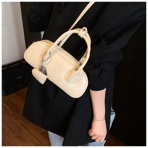 Détail d'un sac bowling crème avec breloque cœur et chaîne argentée sur blazer noir