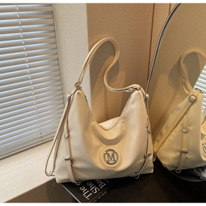Détail d'un sac cabas en cuir crème avec logo M métallique et accents d'anneaux argentés