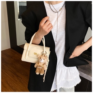 Detail of white crossbody bag with gold hardware and a cute plush bear charm
