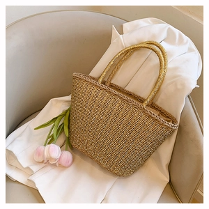 Close-up of champagne gold woven straw tote bag with dual top handles on a grey chair