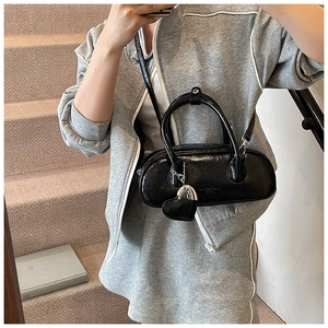 Détail d'un sac à main en cuir verni noir avec pendentif cœur argenté et bandoulière