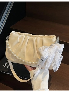 Cream pleated cloud bag with pearl chain and lace bow on a vintage wooden background