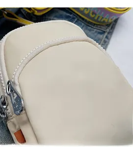 Détail du sac bandoulière en nylon beige avec breloque papillon et sangle large